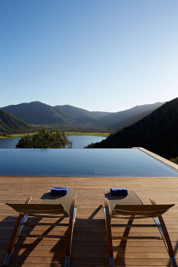 Hladina bazénu zabudovaného do dřevěné terasy splývá s horizontem jezera Humedal de Millahue v pozadí. 