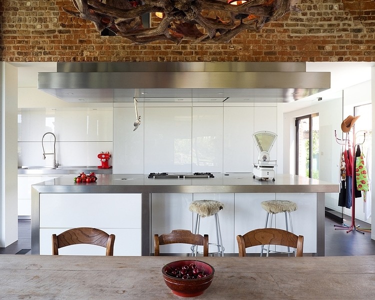 Kuchyňská linka nese strohé a minimalistické tvary, veškeré skřínky jsou bez úchytek. Nadčasový bílý lesk nábytku doplňuje nerez kuchyňského ostrůvku.